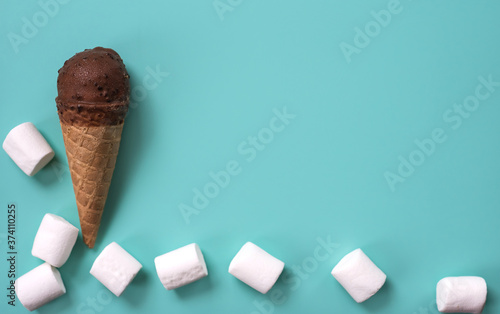 Ice cream-horn with chocolate glaze white small marshmallows against a blue background. Delicious air sweets