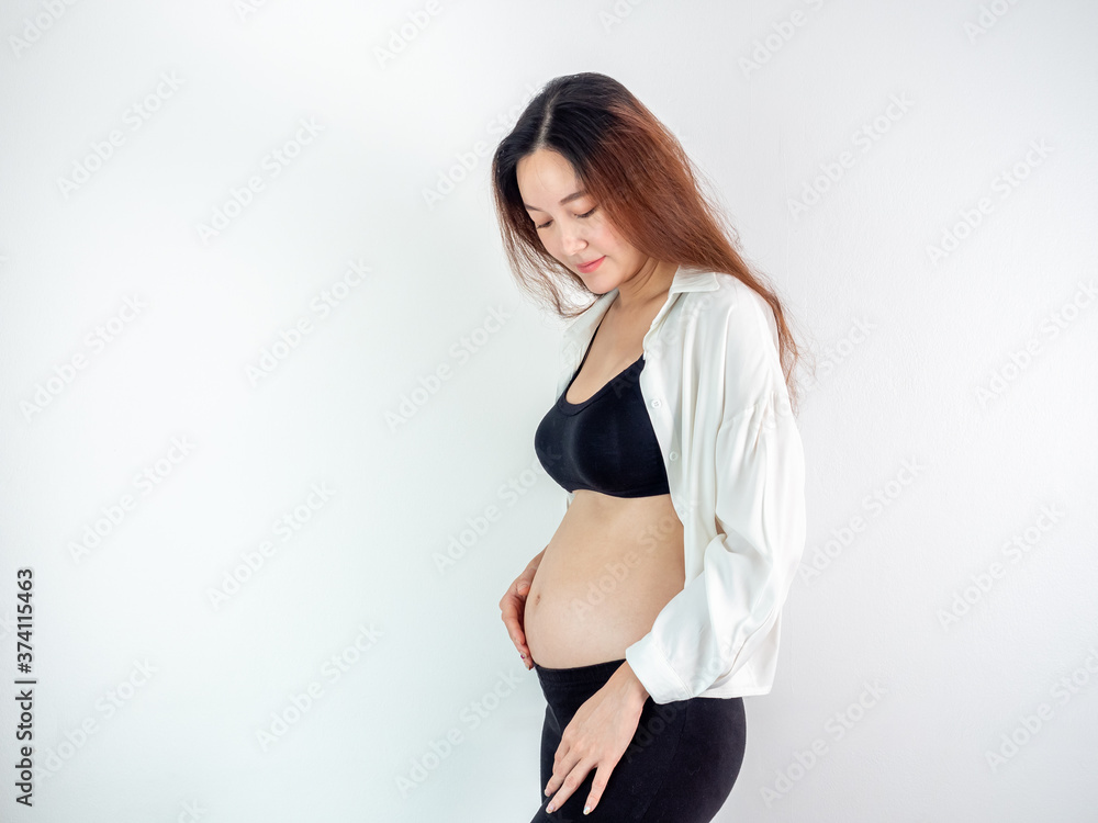 Fototapeta premium portrait of 4 months pregnant Asian woman in white bed room, Woman touching her abdomen belly on white background.