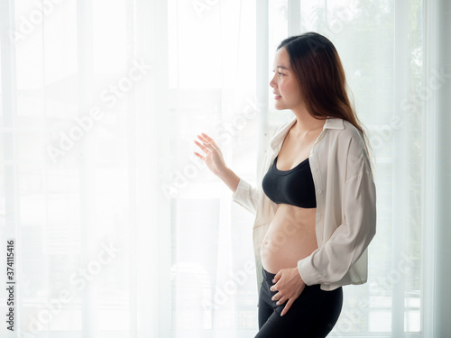 portrait of 4 months pregnant Asian woman in white bed room, Woman touching her abdomen belly on white background. Free Download portrait of 4 months pregnant Asian woman in white bed room, Woman touching her abdomen belly on white background. - GFXLoad