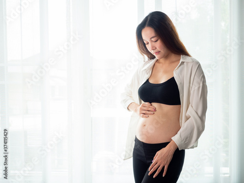 portrait of 4 months pregnant Asian woman in white bed room, Woman touching her abdomen belly on white background. Free Download portrait of 4 months pregnant Asian woman in white bed room, Woman touching her abdomen belly on white background. - GFXLoad