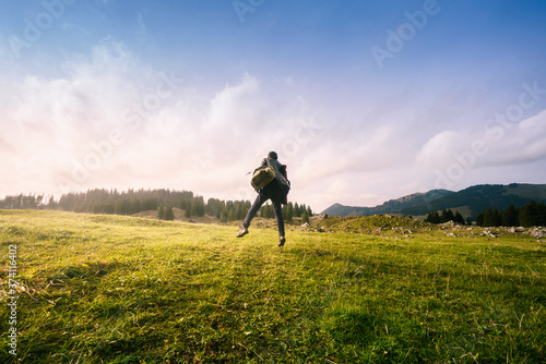 Rare view of only photographer man walking and jumping on grass field in beautiful nature by mountain against sky