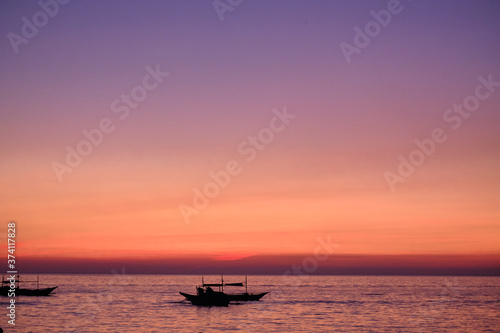 Boracay, Philippines - Jan 27, 2020: Sunset on Boracay island. Sailing and other traditional boats with tourists on the sea against the background of the setting sun. Tourists are sitting on the beach