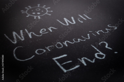 Close up of the phrase When Will Coronavirus End? by handwriting by white coloured chalk on blackboard. The surface of blackboard is powdery and rough.