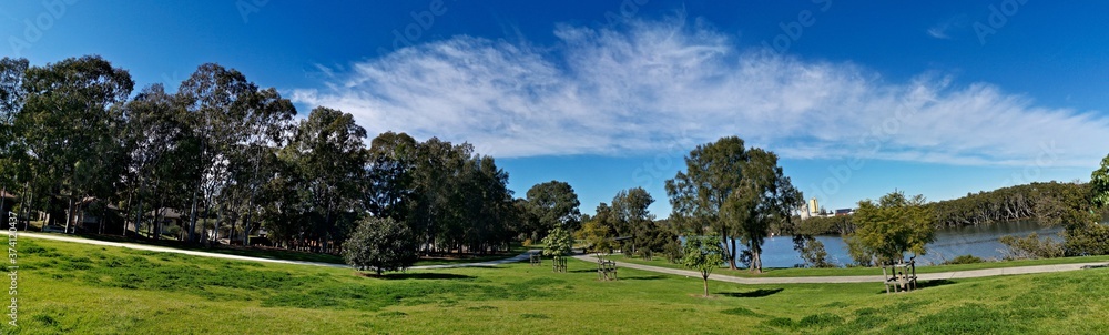 Beautiful panoramic view of a park with green grass, tall trees, walking trail and rainbow look-alike clouds, Reid Park, Parramatta Cycleway, Rydalmere, Sydney, New South Wales, Australia
