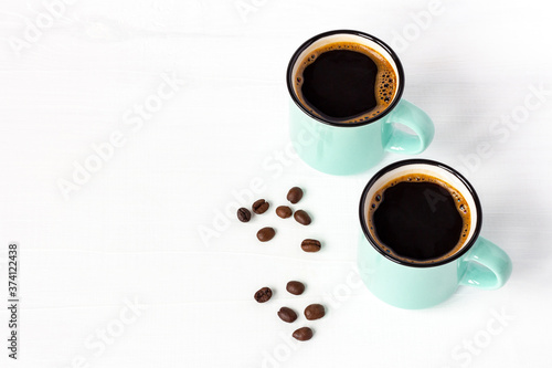 Two azure cups of fresh coffee with grains on white wooden background. Copy space