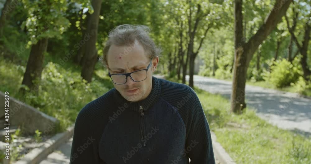 Strange intoxicated male in glasses and with twitching face walking on path on sunny summer day in town Strange intoxicated male in glasses and with twitching face walking on path on sunny summer day in town