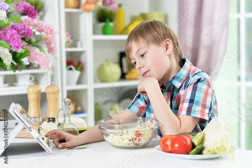 Cute little boy preparing salad and using tablet