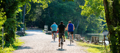 Three men riding bicycles on trail passing a lake in the woods