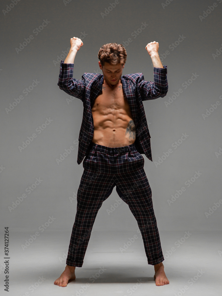Handsome young guy in a wide-open jacket with naked torso stand in studio on gray background Handsome young guy in a wide-open jacket with naked torso stand in studio on gray background