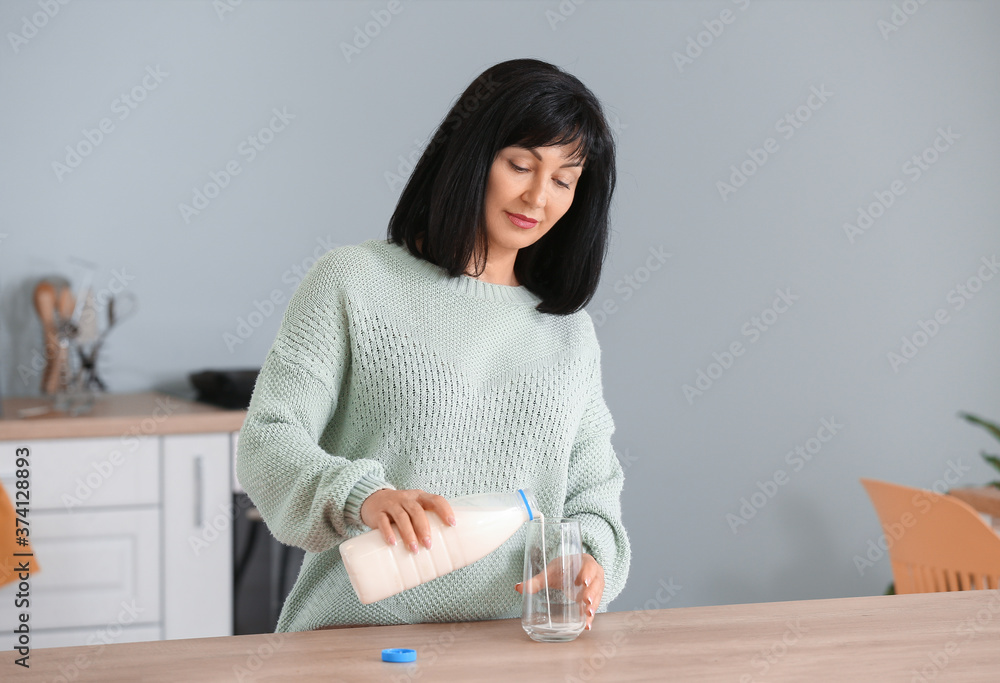 Beautiful mature woman with fresh milk in kitchen Beautiful mature woman with fresh milk in kitchen