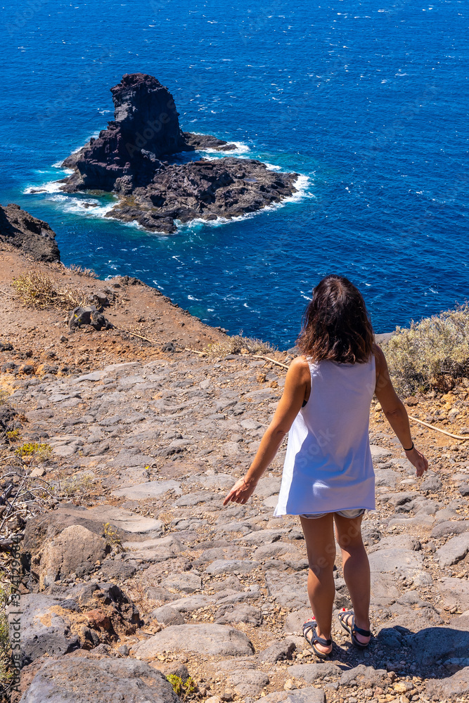 A young tourist walking on the cliff path on the descent to the black sand beach of Bujaren, north of the island of La Palma, Canary Islands. Spain