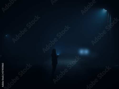 Night city in a thick wet fog . Silhouette of a man with a flashlight walking along the road at night. Headlights of an approaching car. film toning,