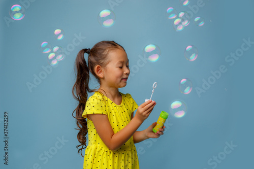 Asian girl playing with soap bubbles in the Studio on a blue background