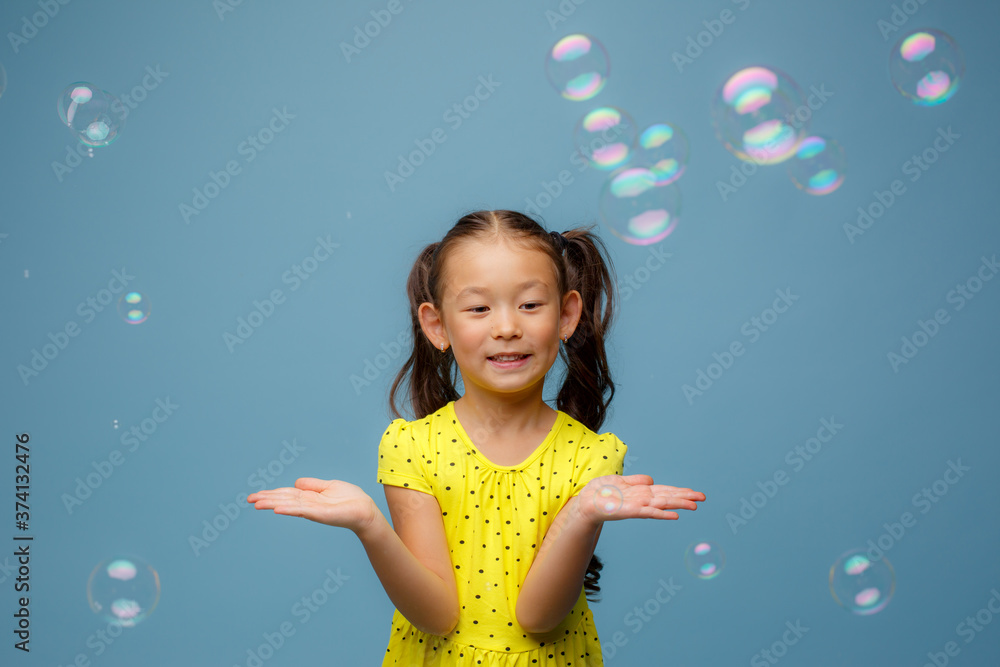 Asian girl playing with soap bubbles in the Studio on a blue background Asian girl playing with soap bubbles in the Studio on a blue background