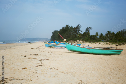 Goa seacoast with colorful boats, palm trees and sandy beach. Weather is windy, nobody is on the beach. India
