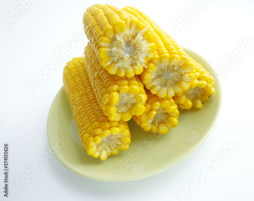 large cobs of ripe corn on a green plate, on a light background. Vitamins, vegetable diet, proper nutrition, healthy and balanced nutrition. A rich harvest from the garden. Wheat corn on a plate close