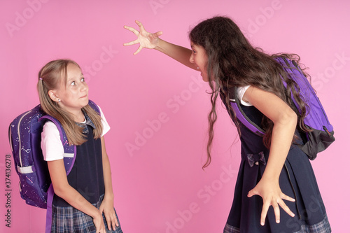 Two schoolgirls in school uniforms are fighting on a pink background