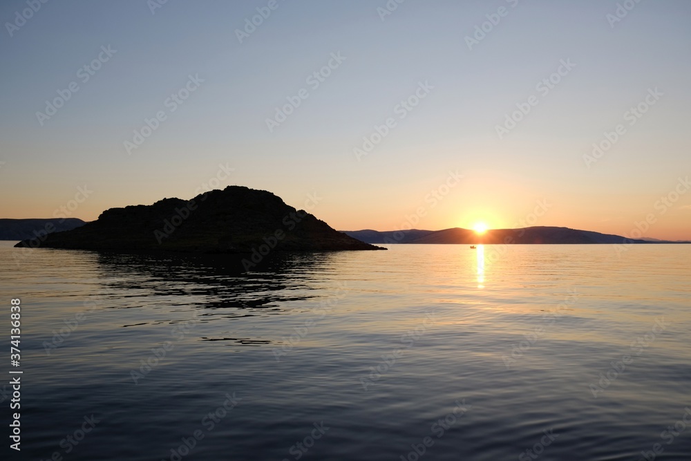 Idyllic landscape with boat on sea at sunset. Rocky island on horizon.
