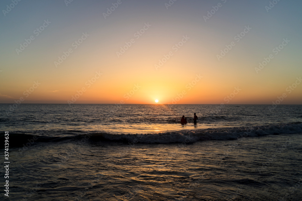 Atardecer en la playa con silueta de nadadores Atardecer en la playa con silueta de nadadores