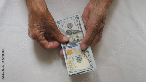 Wrinkled female hands holds cash and counts foreign currency over the table. Arms of elderly grandmother puts one hundred dollar banknotes on the desk. Money concept. Top view Slow motion