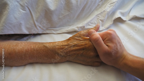 Young man funny takes and comforts hand of his elderly grandmother in hospital. Grandson gently touches wrinkled arm of sick mature woman in medical clinic. Son gives support to his mother. Top view