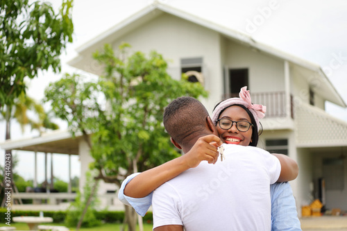 African American wife hugging her husband in front of the house they just move in while holding key for housing, relocation and new family concept