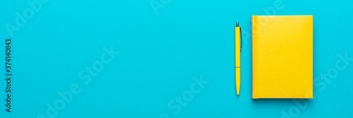 Foto Top view photo of closed yellow notebook and ball-point pen over turquoise blue background with copy space