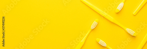 many new plastic yellow toothbrushes in order on the yellow background with copy space
