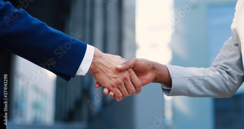 Close up of Caucasian male and African Amercan female hands shaking outdoors. Mixed-races businessman and businesswoman greeting and making deal. Man and woman, business partners meeting. photo