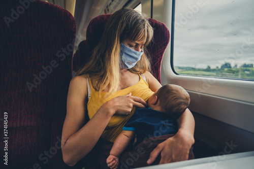 Mother with face mask breastfeeding baby on train