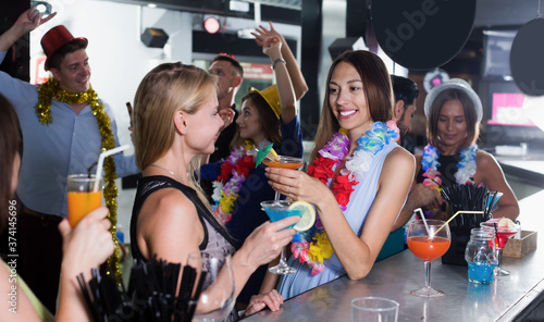 Two positive women have fun and drinking cocktails on hawaiian party..