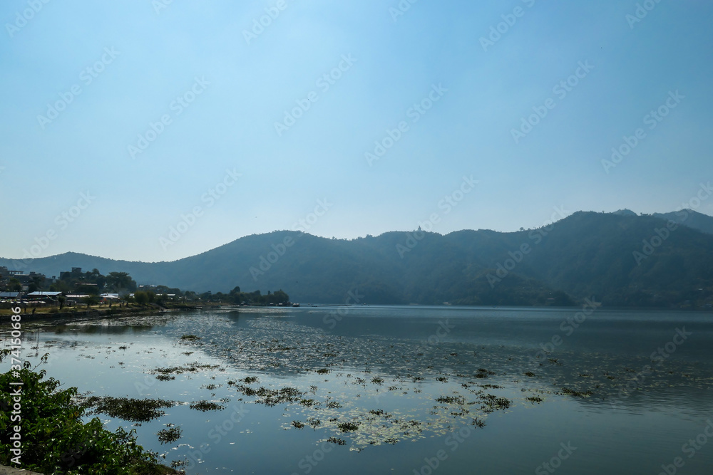 A view on Phewa Lake in Pokhara, Nepal. There are high Himalayan ranges around the lake. Calm surface of the lake. Clear and sunny day. Undisturbed peace. Serenity and relaxation.