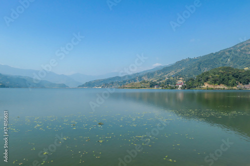 A view on Phewa Lake in Pokhara  Nepal. There are high Himalayan ranges around the lake. Calm surface of the lake. Clear and sunny day. Undisturbed peace. Serenity and relaxation.