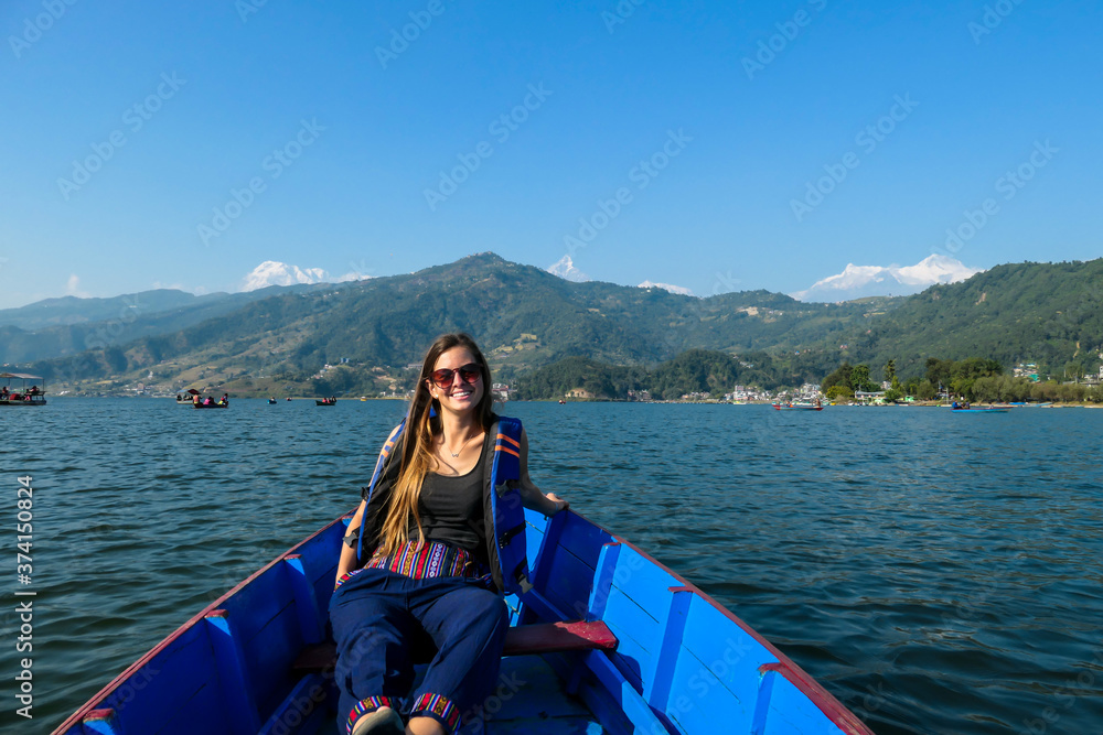 A woman sitting in a blue boat and enjoying a tour across Phewa Lake in Pokhara, Nepal. Behind her there are high, snow capped Himalayas with Mt Fishtail (Machhapuchhare) between them. Relaxation A woman sitting in a blue boat and enjoying a tour across Phewa Lake in Pokhara, Nepal. Behind her there are high, snow capped Himalayas with Mt Fishtail (Machhapuchhare) between them. Relaxation