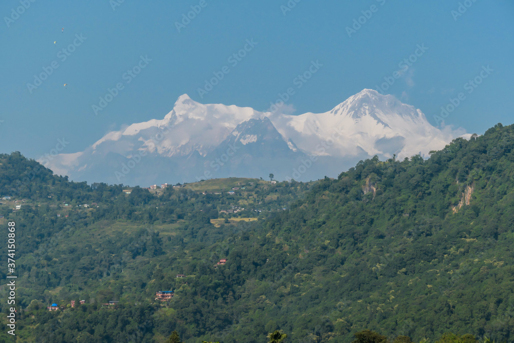Close up view on snow capped Himalayas with Mt Fishtail (Machapuchare) between, seen from Phewa Lake in Pokhara, Nepal. Sharp and dangerous slopes. There is a hill in front of it, covered with forest