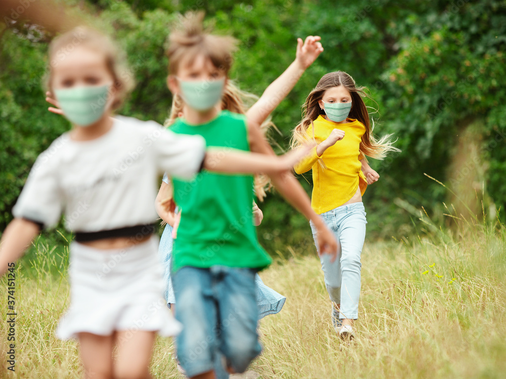Happy little kids wearing protective face mask jumping and running on meadow, forest. Looks happy, cheerful, sincere. Copyspace. Childhood, pandemic concept. Healthcare, coronavirus pandemic.