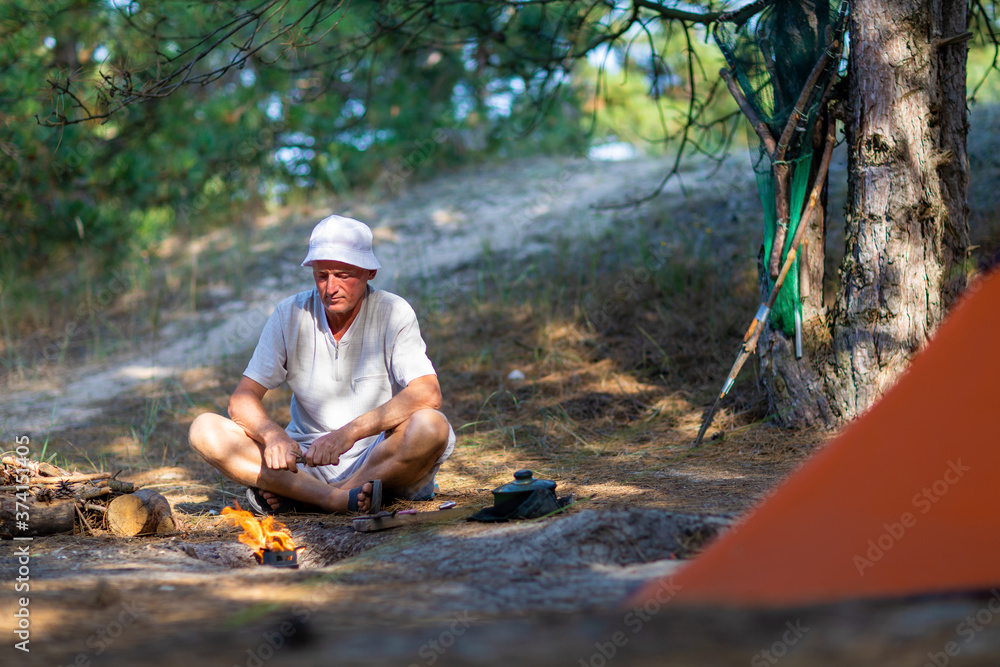 Man looks at a bonfire near a tent in a pine forest Man looks at a bonfire near a tent in a pine forest