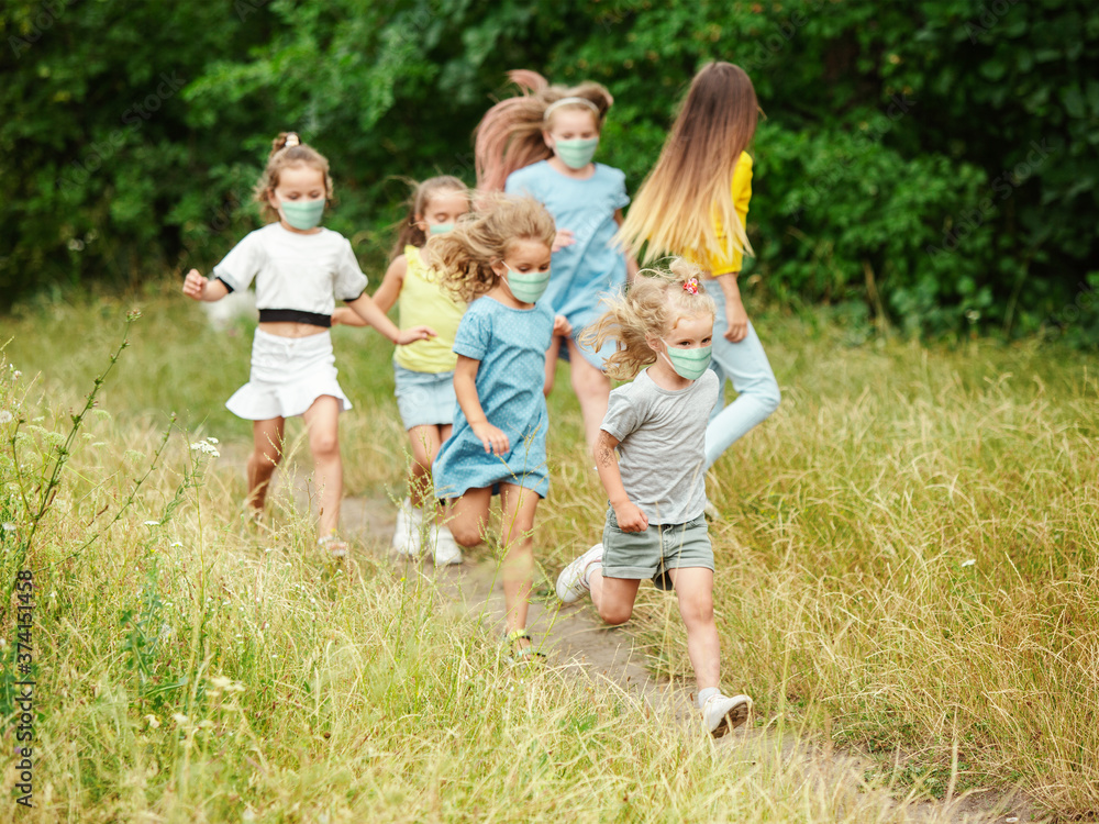 Happy little kids wearing protective face mask jumping and running on meadow, forest. Looks happy, cheerful, sincere. Copyspace. Childhood, pandemic concept. Healthcare, coronavirus pandemic. Happy little kids wearing protective face mask jumping and running on meadow, forest. Looks happy, cheerful, sincere. Copyspace. Childhood, pandemic concept. Healthcare, coronavirus pandemic.