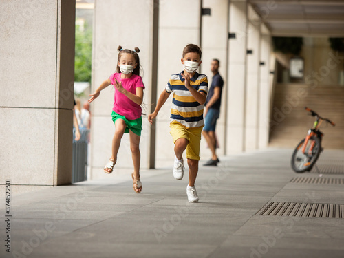 Happy little kids wearing protective face mask jumping and running on city street. Looks happy  cheerful  sincere. Copyspace. Childhood  pandemic concept. Healthcare  coronavirus pandemic.