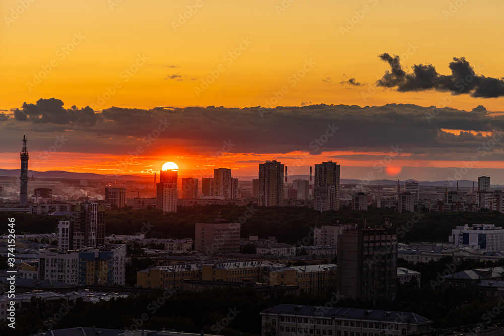 Black silhouettes of buildings are on a red sky background with orange and yellow sunset