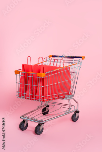 Red shopping bags in trolley on pink surface