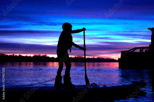 A little boy's silhouette on the SUP (stand up paddle) after sunset against a colorful sky at autumn or winter season