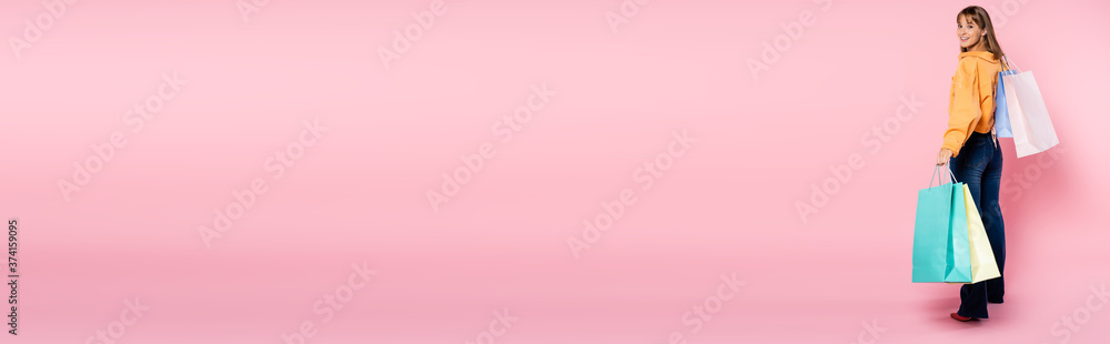Horizontal image of woman with shopping bags looking at camera on pink background with copy space