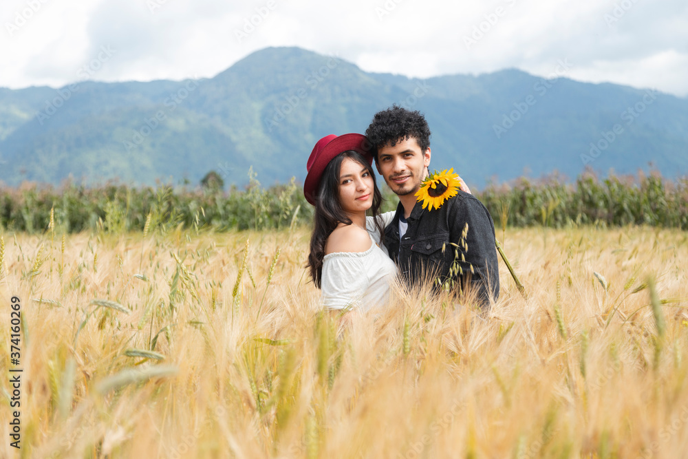 Young Hispanic couple in the middle of a golden wheat field at sunset - Couple in love enjoying the sunset in the middle of nature