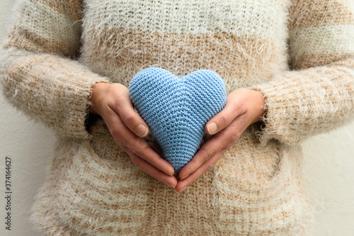 Mulher segurando um coração azul feito em crochê próximo ao ventre. 
