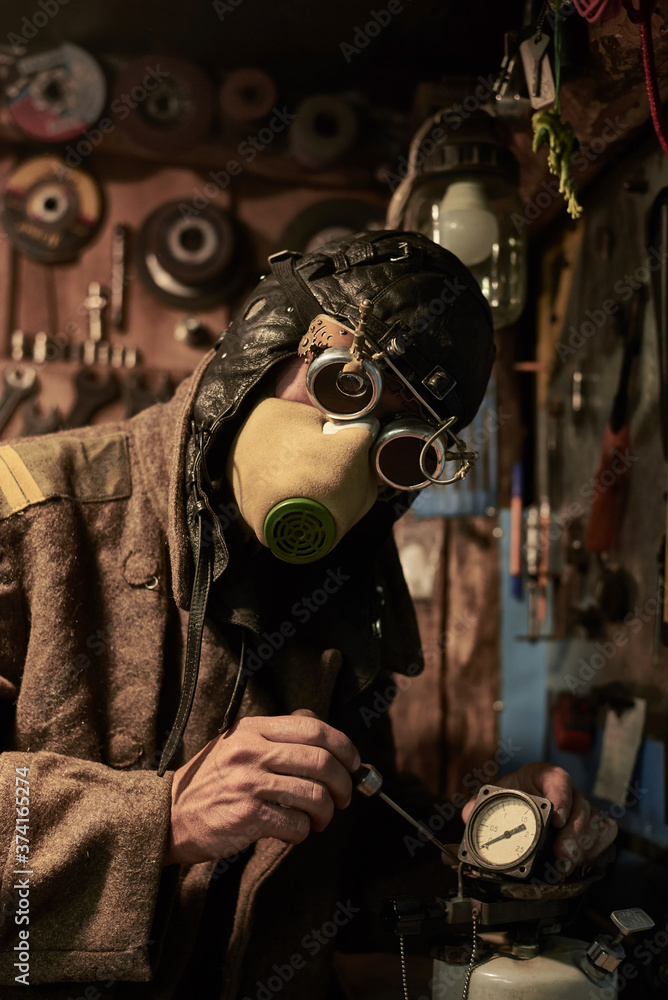 A man in a respirator and glasses in the style of steampunk works with a pressure gauge and a cylinder.