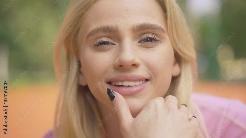 Close-up face of blond young woman with grey eyes smiling at camera. Portrait of charming beautiful Caucasian lady posing outdoor on sunny summer day. Close-up face of blond young woman with grey eyes smiling at camera. Portrait of charming beautiful Caucasian lady posing outdoor on sunny summer day.