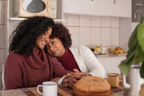 Happy black mother and daughter embracing each other at kitchen table, inside. Togetherness, family, support concept.