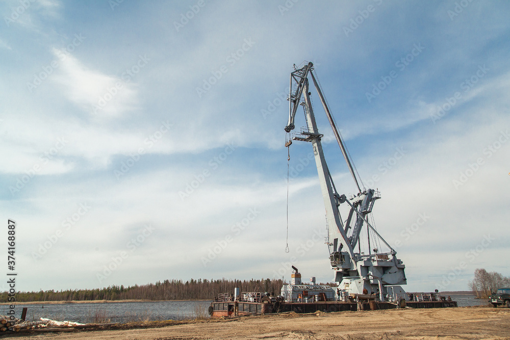 Big industrial ship with crane at river port near pile of logs Big industrial ship with crane at river port near pile of logs