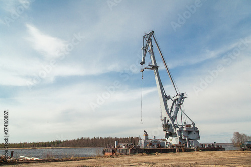 Big industrial ship with crane at river port near pile of logs